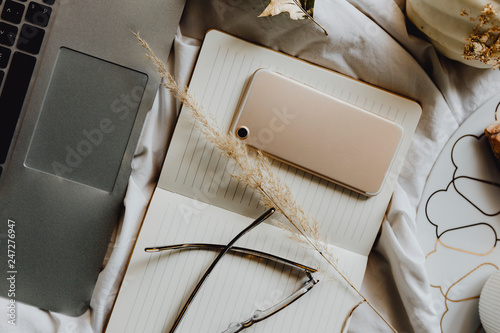 Phone on a notepad next to laptop on a bed photo