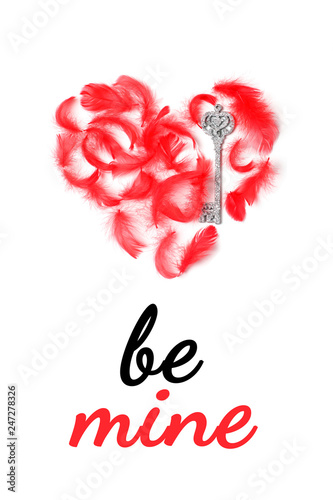 Postcard with the words Be mine in italics. Red heart is laid out of red feathers and decorative silver keys. Top view, flat lay, vertical format photo