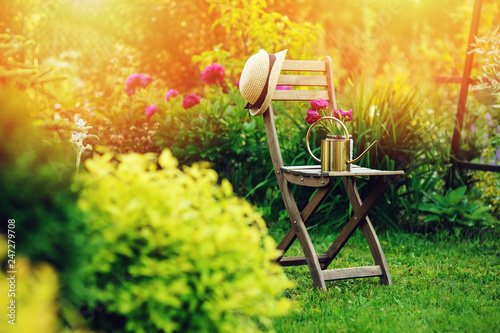 beautiful blooming summer private garden with wooden chair, gardener hat and watering can