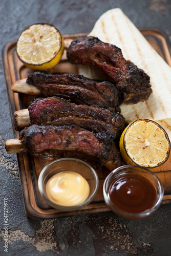 Close-up of bbq beef ribs with dipping sauces, lemon and tortillas, selective focus, vertical shot