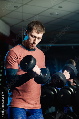 Handsome athletic man trains biceps with dumbbells in the gym.