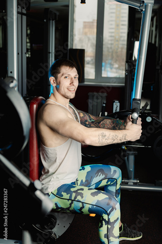 Handsome athletic man trains pectoral muscles on a simulator in the gym.