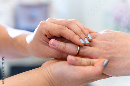Wedding theme, Bride putting ring on groom hand, and they holding hands with a nice manicure neat. Close up hands of man and woman put wedding ring on hand.