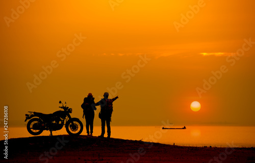 Silhouette Couple with a motorbike at river side at sunset.