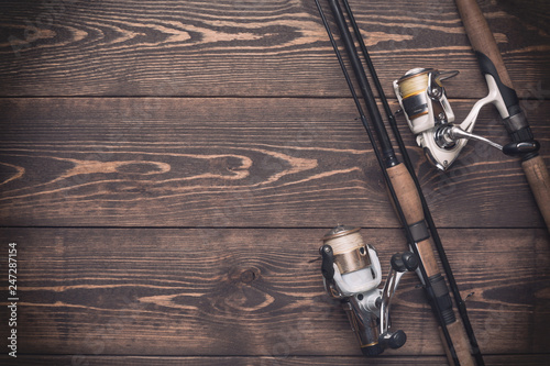 Fishing concept. Fishing spinning rods and reels with lines on wooden background with free space.