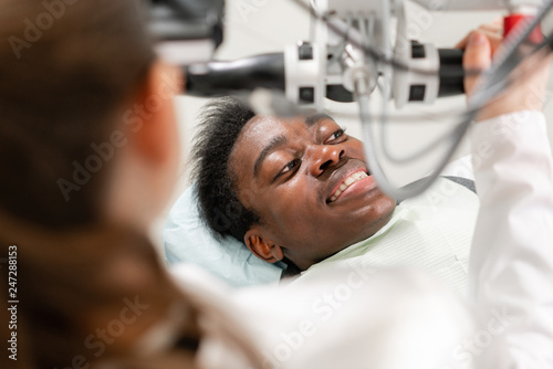 Young African American male patient at chair at dental clinic. Medicine, health, stomatology concept. dentist conducts inspection and concludes