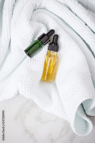 Zwei Flaschen mit Naturkosmetik Serum Grün und Beauty Öl Gelb für Gesicht Haut Schönheit Kosmetik und Pflege an Handtücher auf Marmor Hintergrund