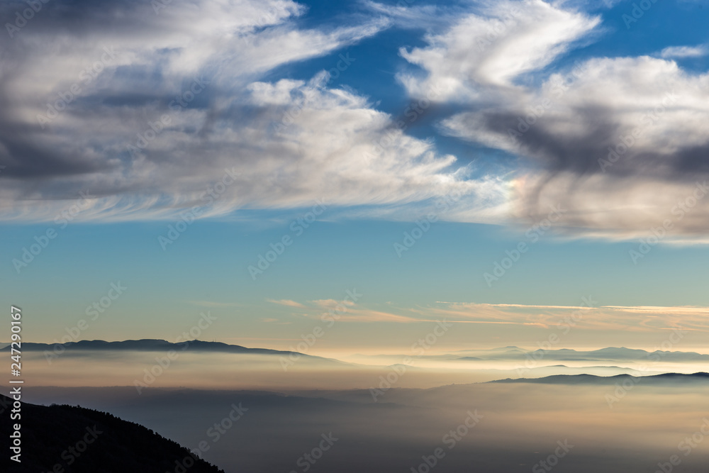 Valley filled by fog with blue sky with clouds and warm sunset colors