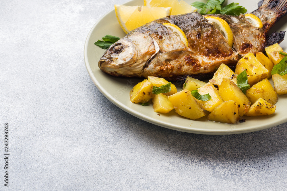 Baked fish carp with lemon greens and potatoes on a plate. Copy space Baked fish carp with lemon greens and potatoes on a plate. Copy space