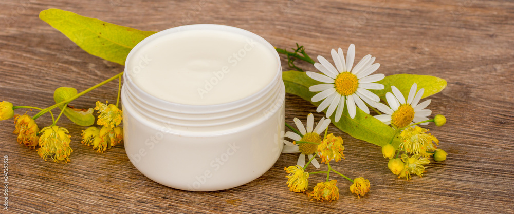 body cream opened plastic jar with chamomile and linden flowers on wooden table body cream opened plastic jar with chamomile and linden flowers on wooden table