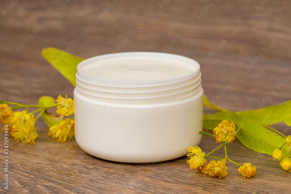 body cream opened plastic jar with chamomile and linden flowers on wooden table body cream opened plastic jar with chamomile and linden flowers on wooden table