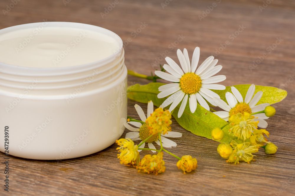 body cream opened plastic jar with chamomile and linden flowers on wooden table body cream opened plastic jar with chamomile and linden flowers on wooden table