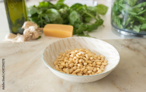 Close up of pine nuts in small dish on marble board with ingredients for basil pesto in background (selective focus)
