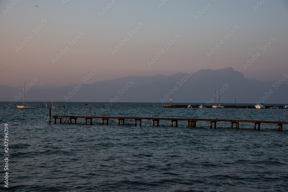 Wooden pier and concrete pier for mooring boats on the lake. Beautiful winter sunny day with grazing light. Some boats are docked at the dock. A sailboat in the middle of the lake. Background with mou