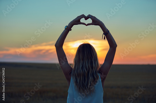 Girl holding heart-shape symbol for love in sunset / sunrise time.