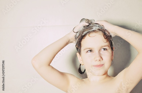 Young European girl in bubble bath, looking up and shampooing her hair 