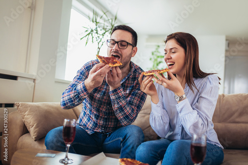 Beautiful young couple eating pizza talking and smiling at home.