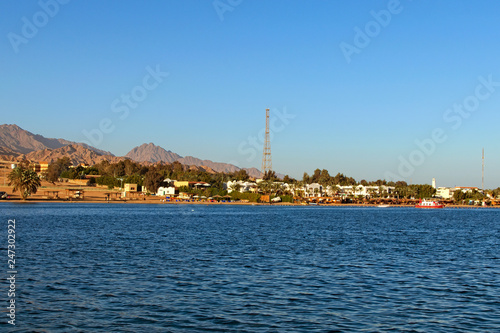 Beautiful landscape view of the Red Sea shore, beach with some buildings, sand. High mountains at the background. Summer vacation concept. Red Sea, Dahab, Egypt