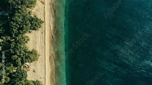 stunning aerial drone minimal geometric footage of a remote tropical sea ocean shore with sandy beach lush rainforest jungle and crystal clear azure blue water from top looking down at sunset