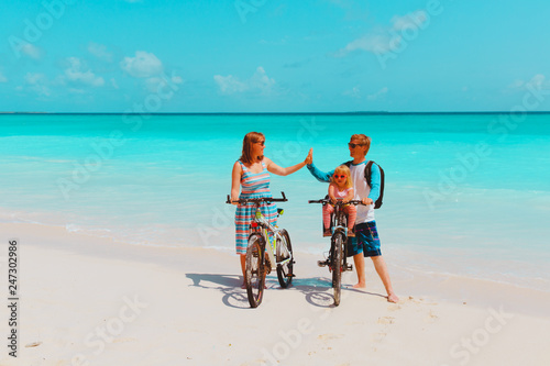 happy family with little baby girl riding bikes on beach