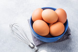 Brown raw Chicken eggs in a blue bowl on a grey background.