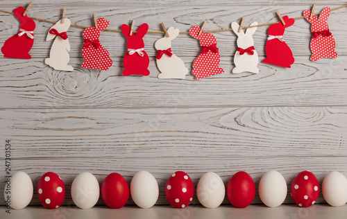 Happy Easter! Painted Easter eggs and Easter decoration - Easter bunnies with ribbons - red, white and red with white polka dots on a gray wooden background.