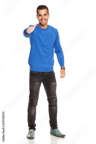 handsome happy young man in blouse and jeans on white background showing thumbs up