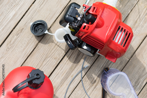 lawn mower and red canister with gasoline lie on a wooden background
