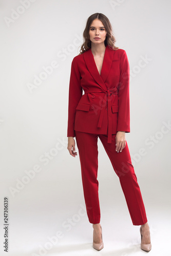 young elegant woman in red trouser suit standing in the studio on gray background
