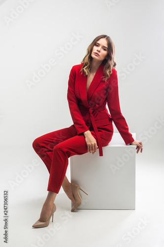 vogue model seating on white cube in red elegant suit