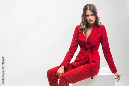 vogue model seating on white cube in red elegant suit
