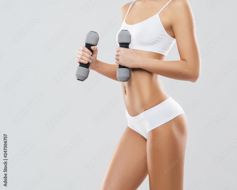 Fototapeta premium Young and fit girl pumping a dumbbells. Woman in sporty swimsuit. Sport, fitness and healthy lifestyle concept.