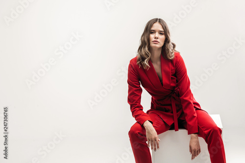 vogue model seating on white cube in red elegant suit