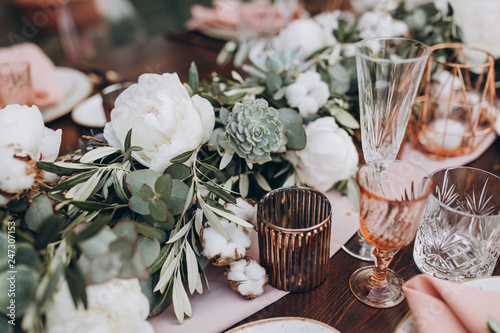 on wooden banquet table are glasses, plates, candles, table is decorated with compositions of cotton and eucalyptus branches