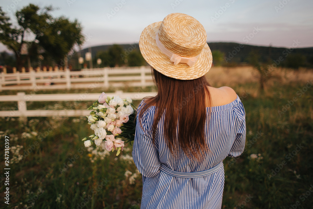 Back view of Beautiful lady. She hold a bouquet of flowers and smile. Background of farm