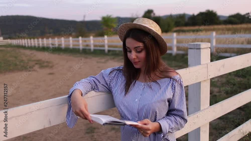 Beautiful pregnant woman read the book on the farm. She stand by the fance and look in to the book. Relax
