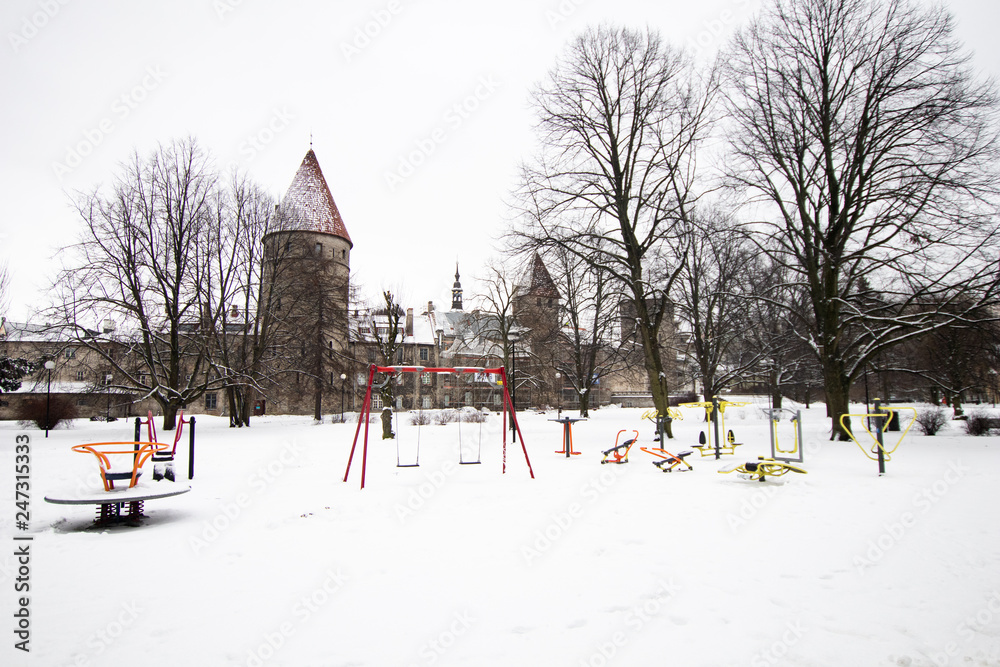 Naklejka premium towers and medieval walls of the city of Tallinn in Estonia, with a playground for children in the middle of frozen snow. Life in winter in the Baltic countries, in Estonia