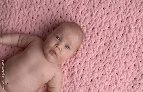 the baby lies carelessly and looks at the camera in surprise. The baby lies on a pink micro-polyester rug. photo