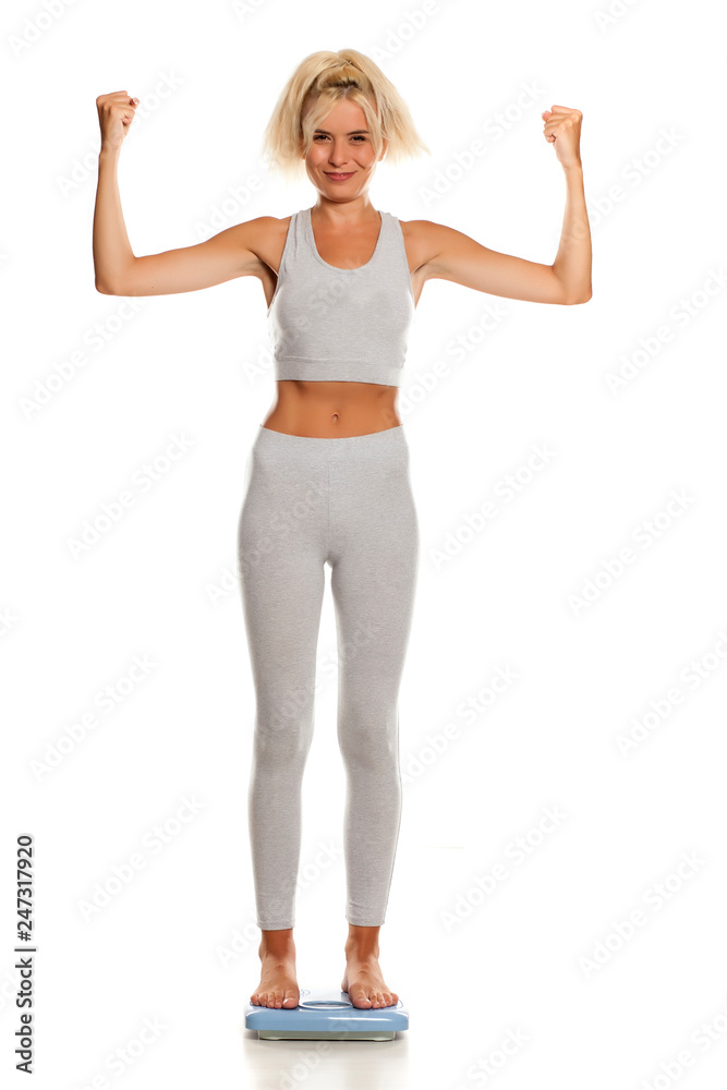 slim sporty young woman in gray leggings standing on a scale on white background slim sporty young woman in gray leggings standing on a scale on white background