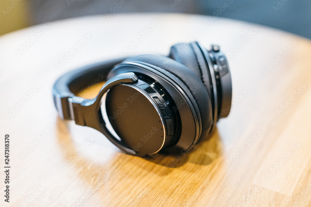 Picture of black wireless headphones on wooden table/ high-quality expensive headphone, natural materials, music time, selective focus on headset, top view with copy space/ music and lifestyle concept