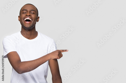 Happy african man laughing out loud at funny joke pointing finger aside at copy space, jovial cheerful black guy burst with laughter joy having fun advertising isolated on white studio background