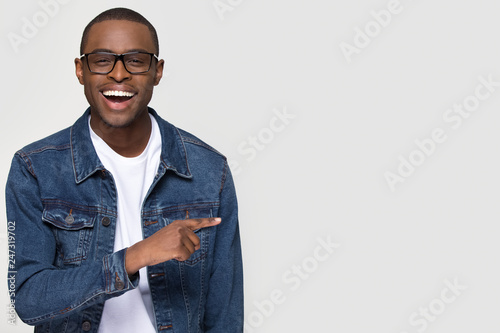 Happy excited african man customer laughing pointing finger aside at copy space, cheerful black guy advertising fun optics denim shop or dental service sale offer isolated on white studio background