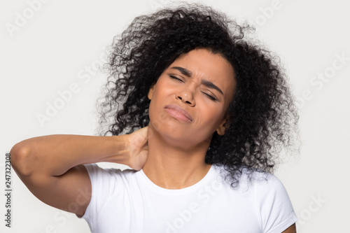 Tired upset african young woman massaging hurt stiff neck isolated on white grey studio background, fatigued sad black lady rubbing tensed muscles to relieve joint shoulder pain, fibromyalgia concept photo