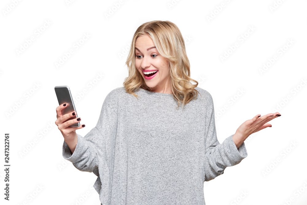 Excited young woman looking at her mobile phone smiling and celebrating in disbelief. Woman reading positive text message on her phone, isolated over white background. Excited young woman looking at her mobile phone smiling and celebrating in disbelief. Woman reading positive text message on her phone, isolated over white background.