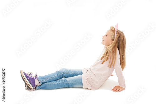 Beautiful little girl sitting on floor, looking on copy space. Isolated on white background