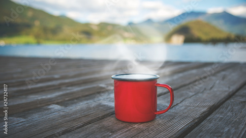 concept adventure, camping, outdoors, individual travelling: red mug on wooden floor in front of a fjord