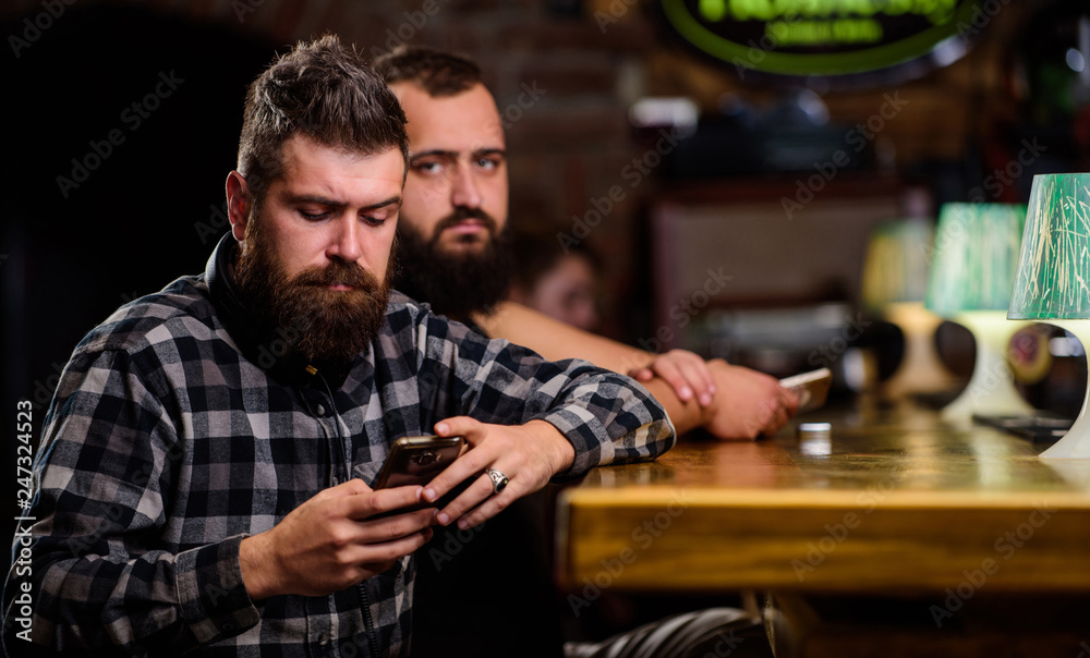 Order drinks at bar counter. Men with smartphone relaxing at bar. Mobile dependence concept. Mobile phone always with me. Friday relaxation in bar. Hipster bearded man spend leisure at bar counter