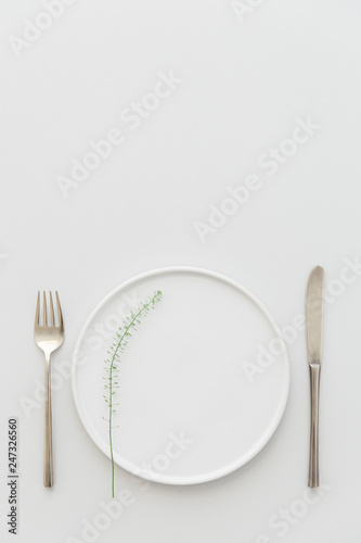 Minimal grey and white table setting with a brass cutlery set, a plate decorated with greenery.