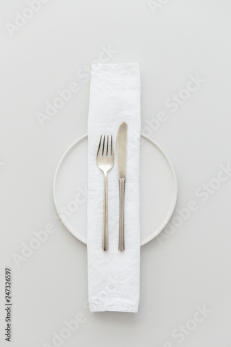 Minimal grey and white table setting with a brass cutlery set, a plate and a white napkin.