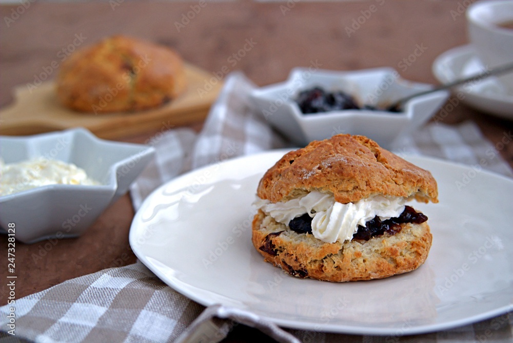Traditional English scones with dried cranberries on a white plate. Served with jam and whipped cream.
